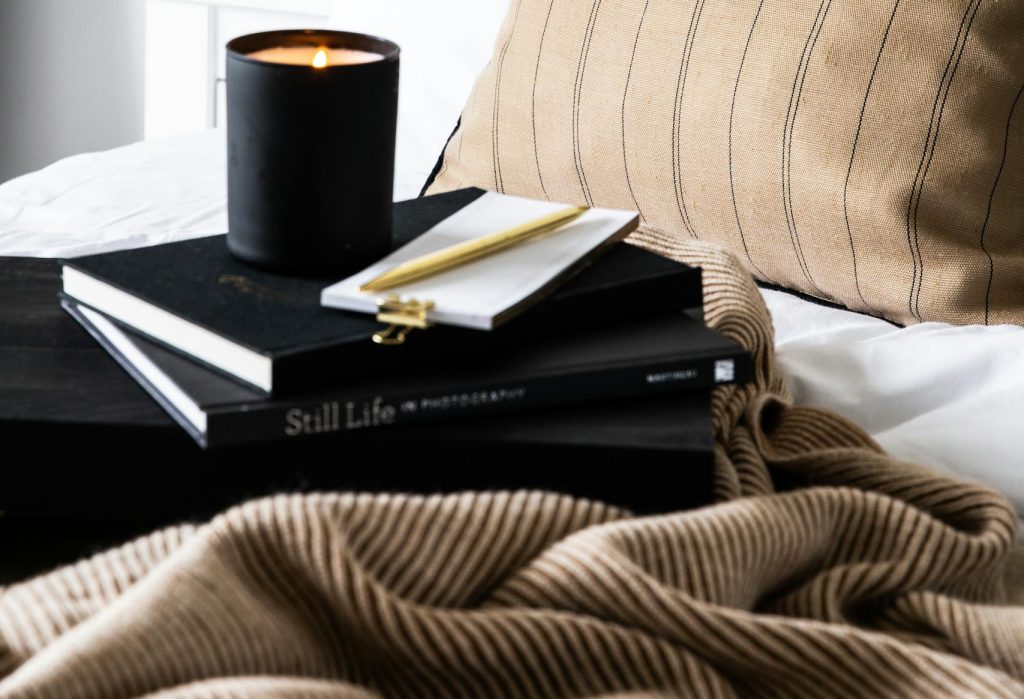 A cozy bedroom scene with a candle, books, and blanket on a bed.