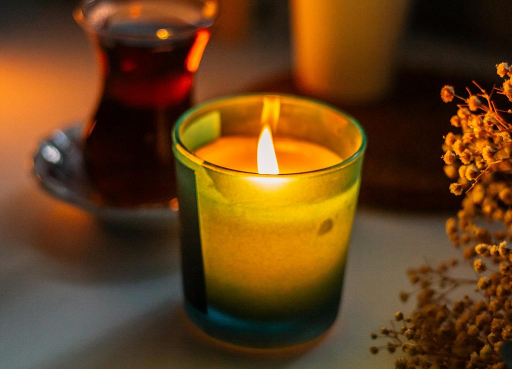A lit candle creates a warm ambiance beside a cup of tea on a cozy evening setting.