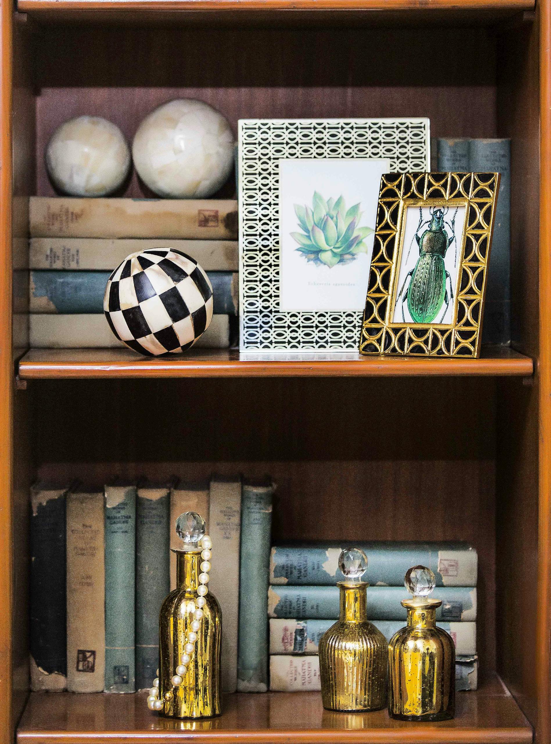 A vintage bookshelf featuring antique books, decorative frames, and golden bottles, creating a sophisticated indoor decor.